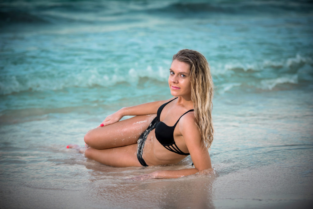 Model strikes a sultry pose laying on her side in the sand in front of the Caribbean Sea