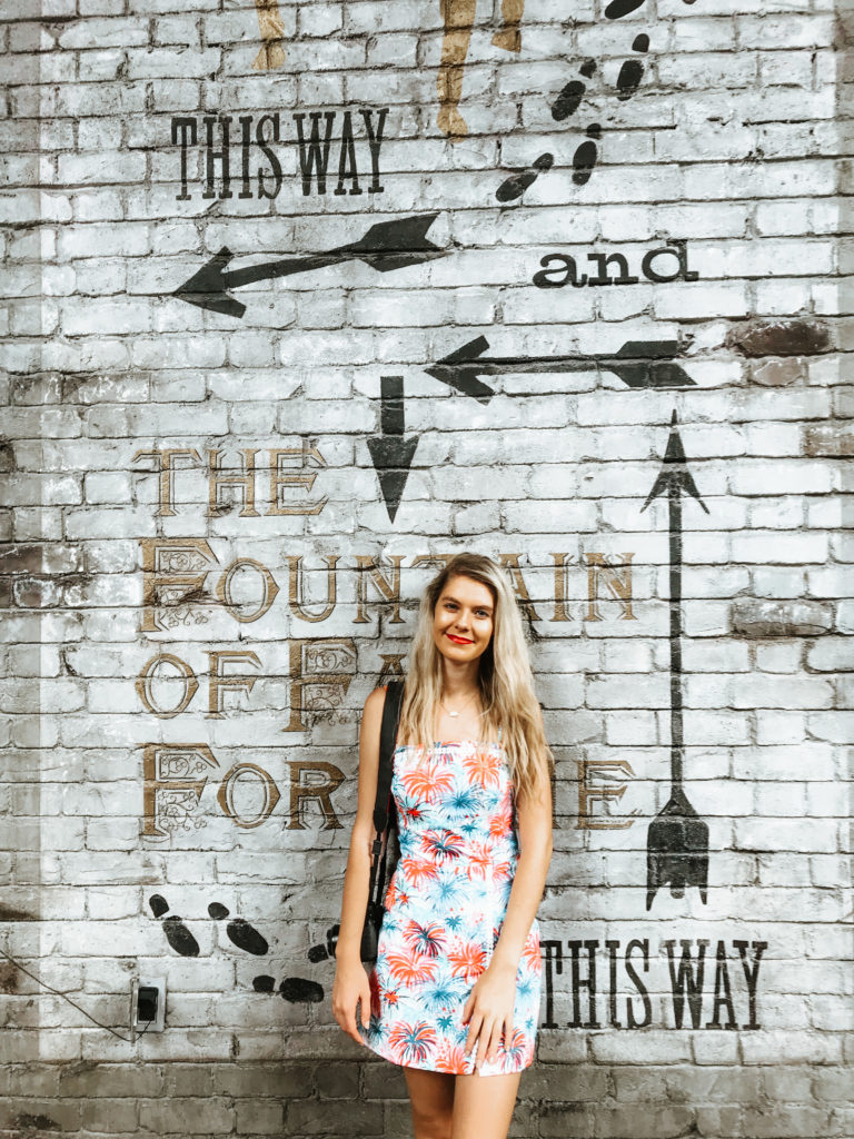 Girl in a Lilly Pulitzer dress stands in front of a mural wall for the Fountain of Fair Fortune