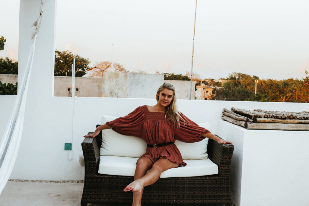 Girl poses with one leg extended while sitting on patio furniture on a white rooftop deck