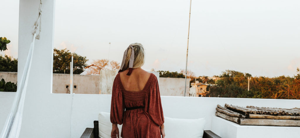 Girl wearing a hair scarf looks out from a white rooftop over Tulum Pueblo